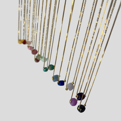 Set of thin gold chains with colorful beads on a white background
