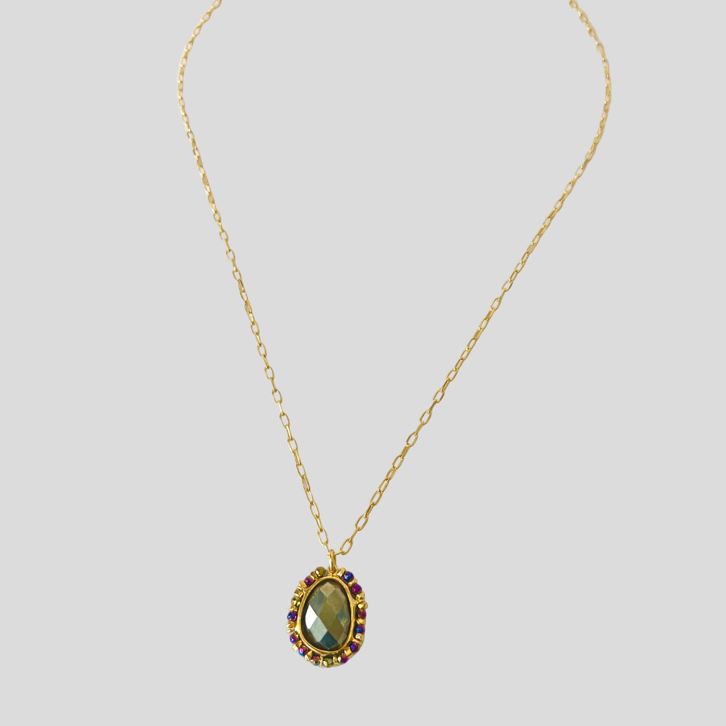 Gold necklace with a green gemstone pendant on a white background