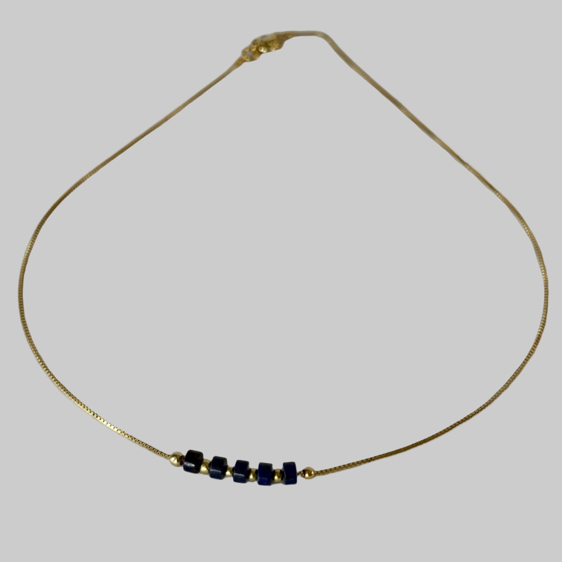 Gold necklace with blue beads on a light gray background