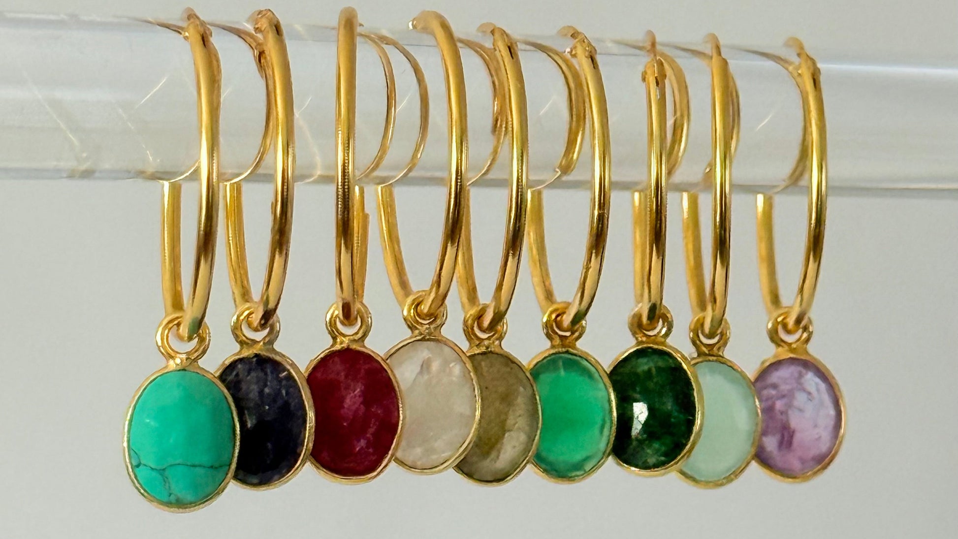 Gold hoop earrings with colorful gemstones on a white background