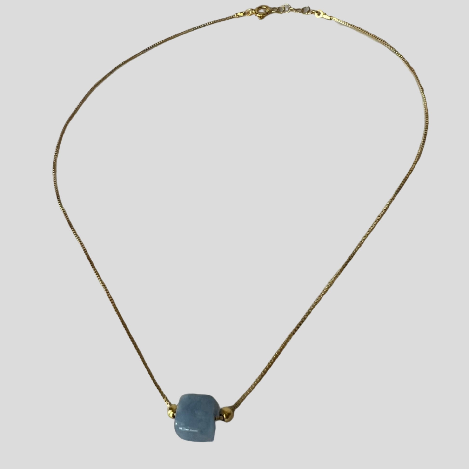 Gold necklace with a blue pendant on a light gray background