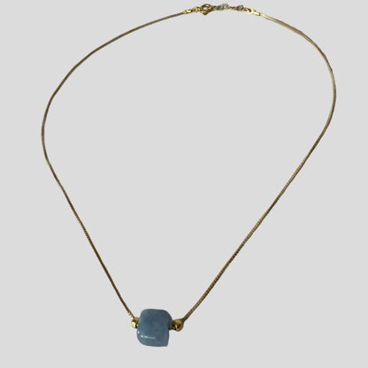 Gold necklace with a blue pendant on a light gray background
