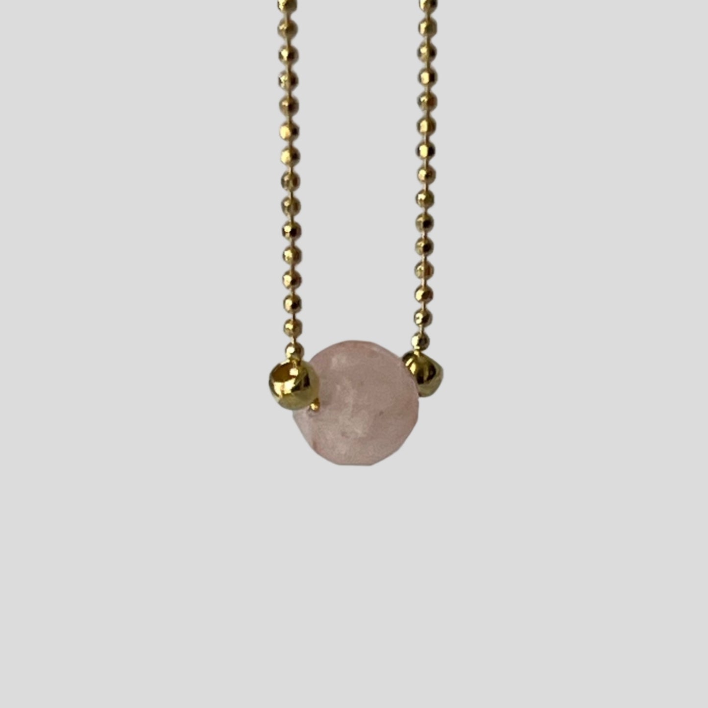 Necklace with a pink gemstone pendant on a gold chain against a gray background