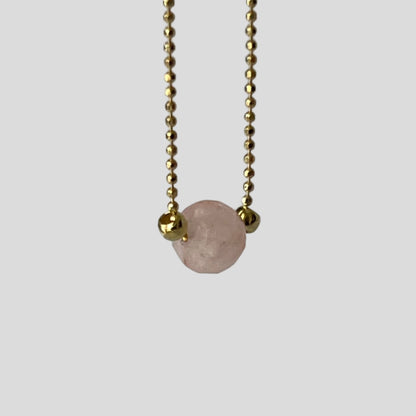 Necklace with a pink gemstone pendant on a gold chain against a gray background