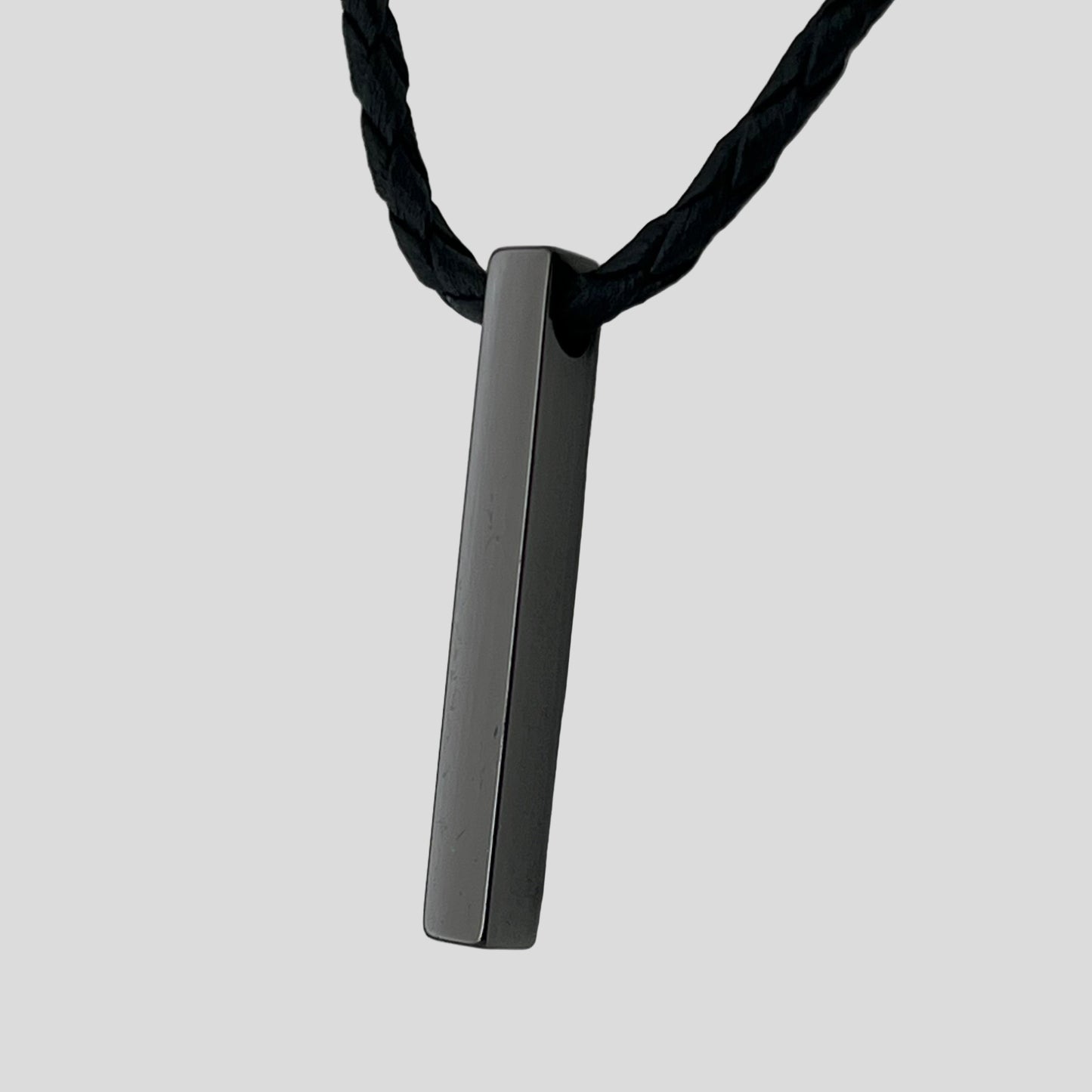 Black rectangular pendant on a black cord against a light gray background