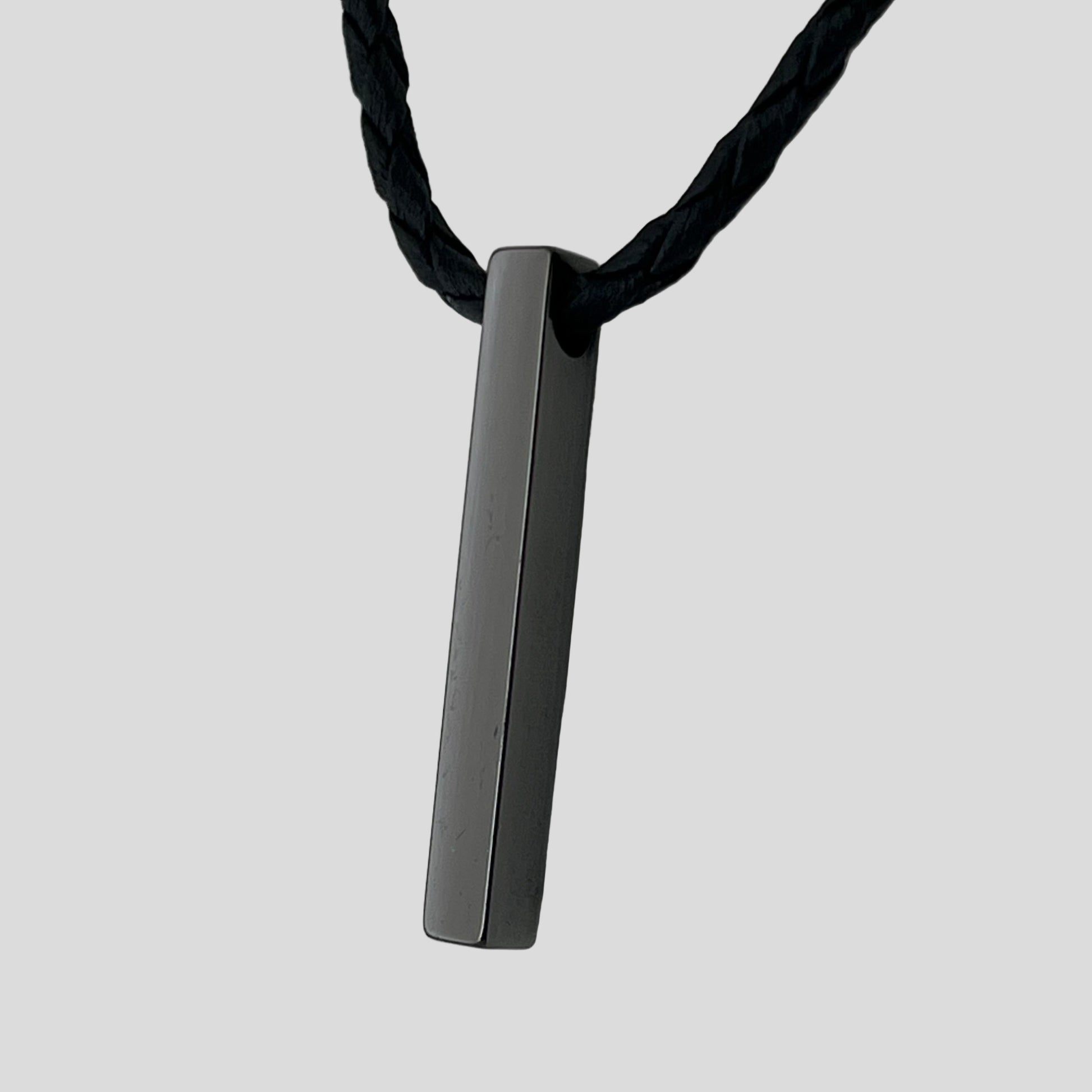 Black rectangular pendant on a black cord against a light gray background