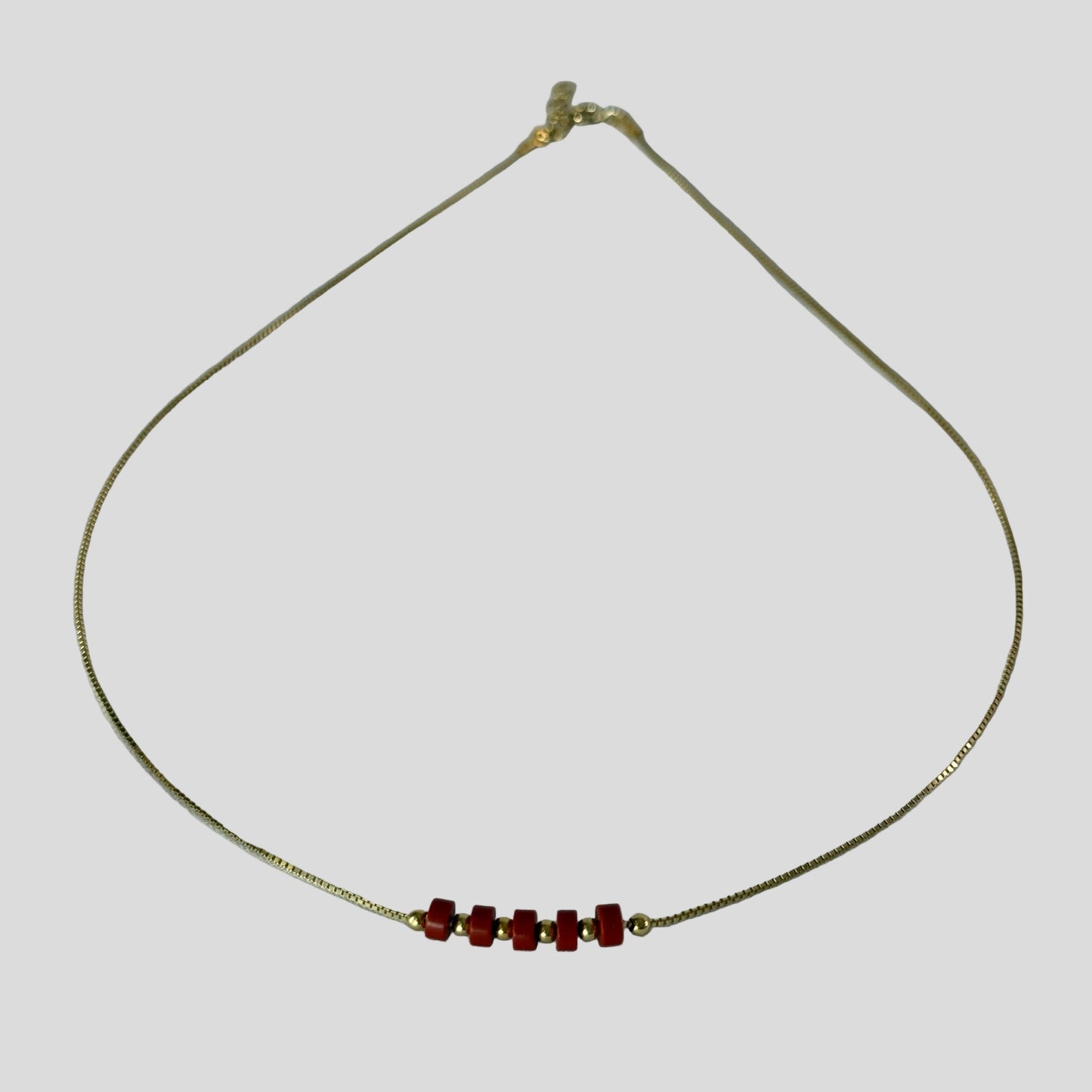 Gold necklace with red beads on a light gray background