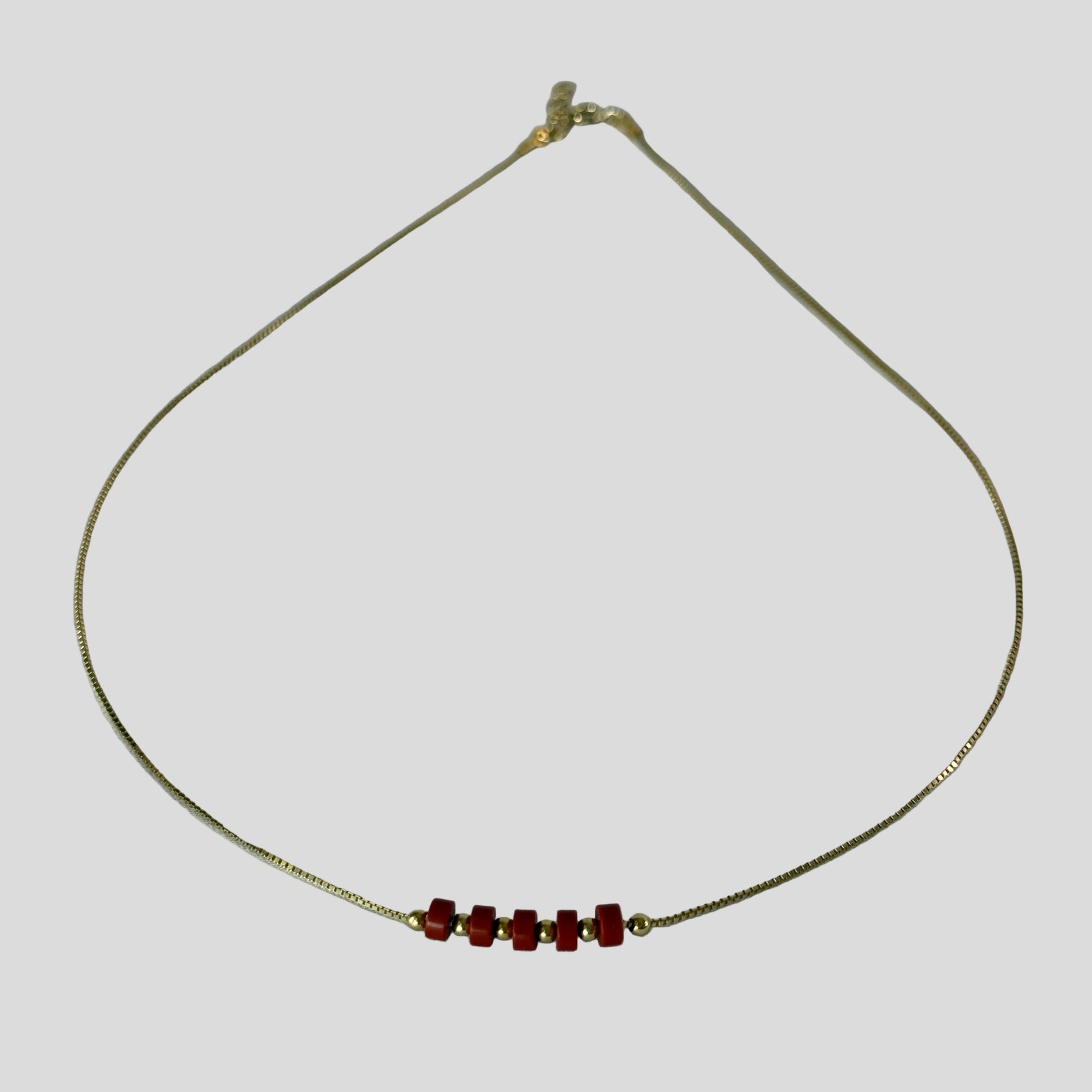 Gold necklace with red beads on a light gray background