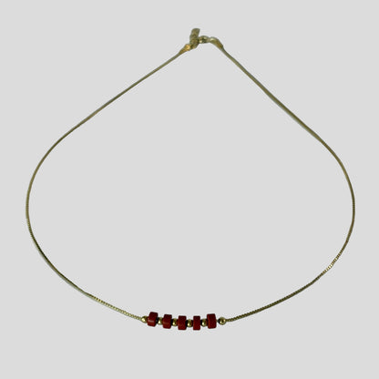 Gold necklace with red beads on a light gray background