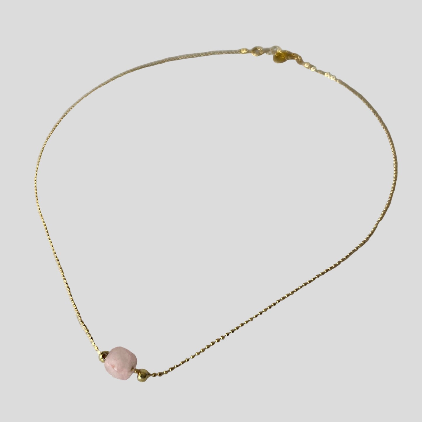 Gold necklace with a pink bead on a light gray background