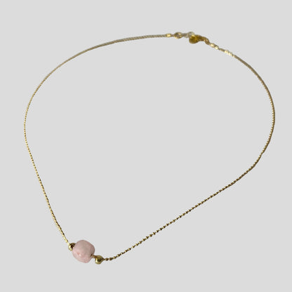 Gold necklace with a pink bead on a light gray background