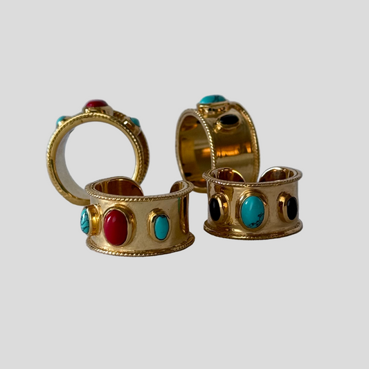 Gold rings with colorful gemstones on a light gray background