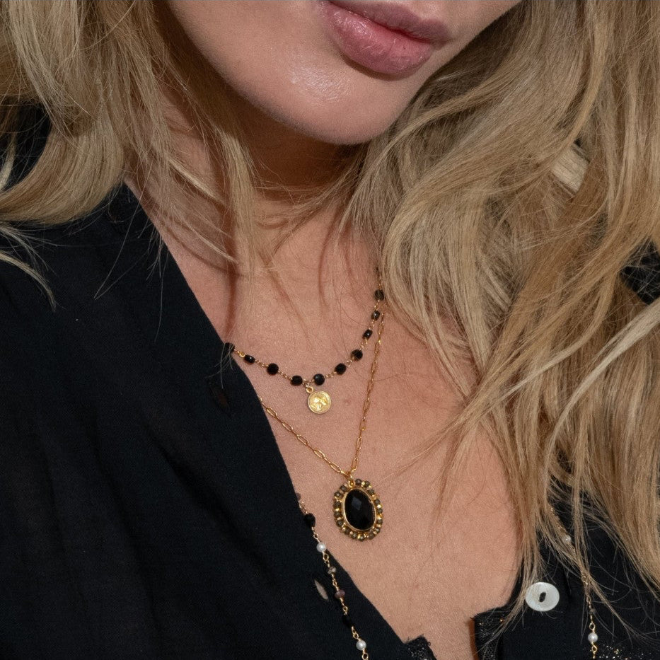 Person wearing layered necklaces and holding a book with a colorful cover.