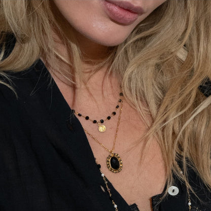 Person wearing layered necklaces and holding a book with a colorful cover.